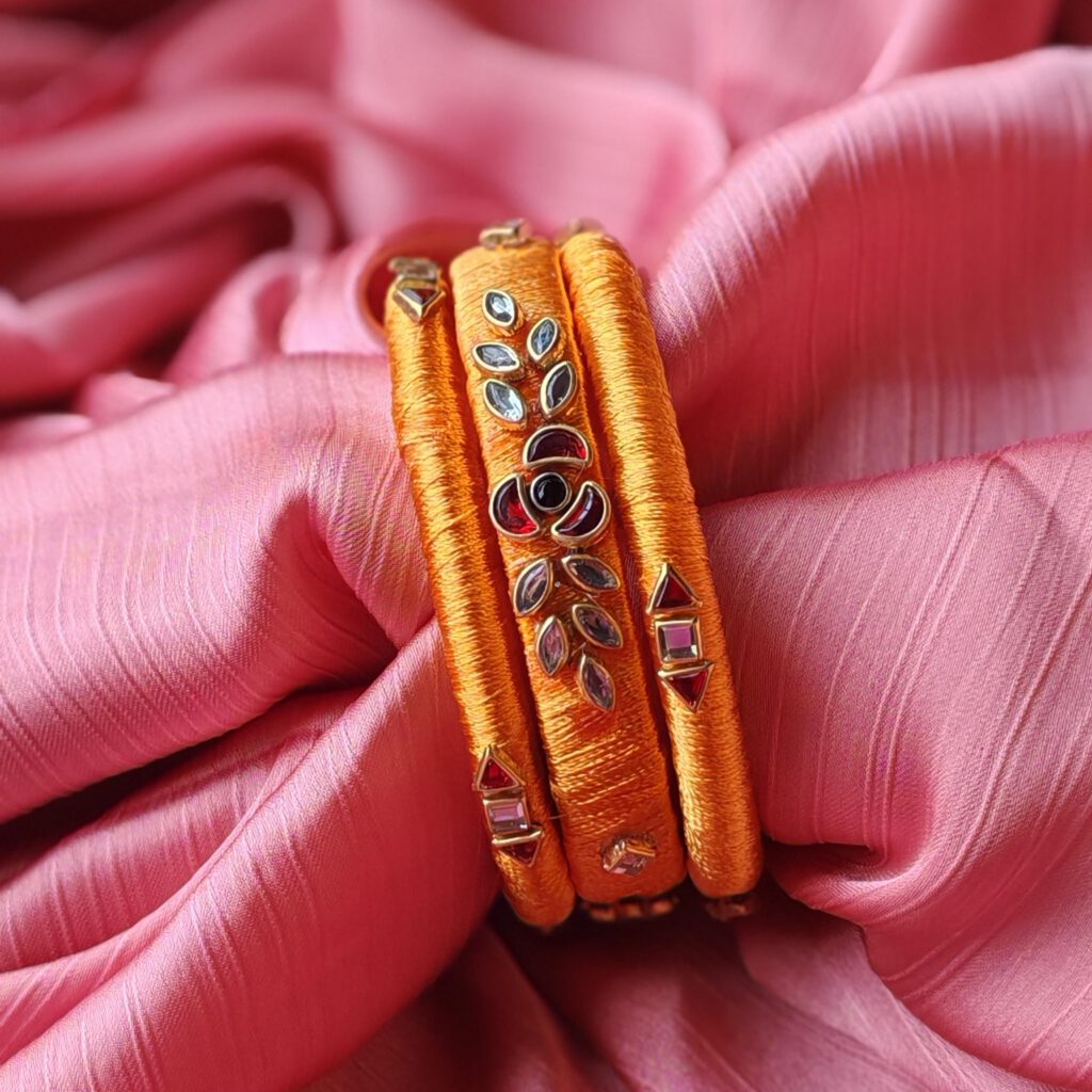 Orange silk thread bangles with kundan stones on pink fabric